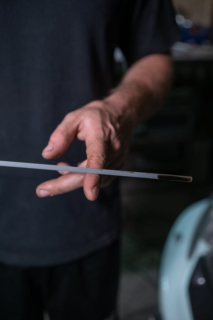 Detailed close-up of a hand holding a dipstick to check engine oil level in a garage setting.